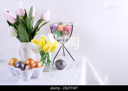 Congratulation Easter card of served table with spring flowers and handmade painted eggs against light grey wall. Stock Photo