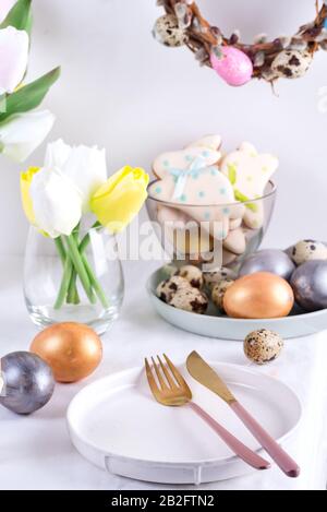 Easter table setting with tulips, easter eggs, cookies and plate with cutlery on white table Stock Photo