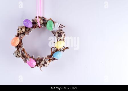 Handcraft Easter wreath made from willow twigs and painted eggs against a light grey background. Stock Photo
