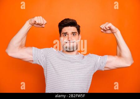 I can do it. Photo of self-assured guy raise fists arms showing strong biceps pushing hard diligent sportsman wear striped t-shirt isolated vibrant Stock Photo