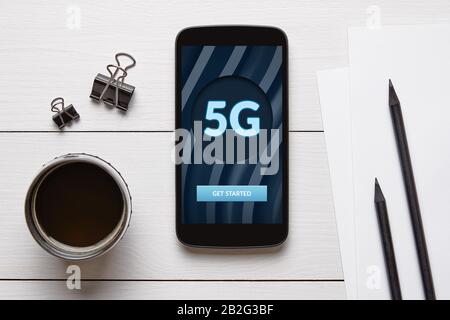 5G network concept on mobile phone screen with office objects on white wooden table. Top view Stock Photo