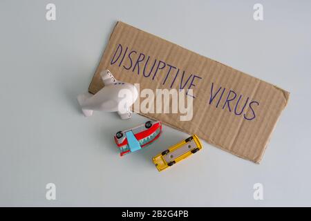 Cardboard sign with message DISRUPTIVE VIRUS, buses and plane model turned upside down. Covid 19 outbreak destroying tourism and world economy Stock Photo