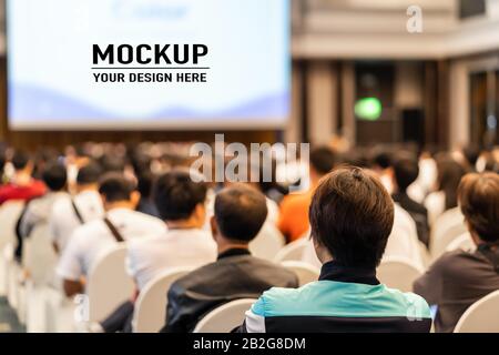 Rear view of Audience listening Speakers on the stage with presentation via projector in the conference hall or seminar meeting and workshop event, bu Stock Photo