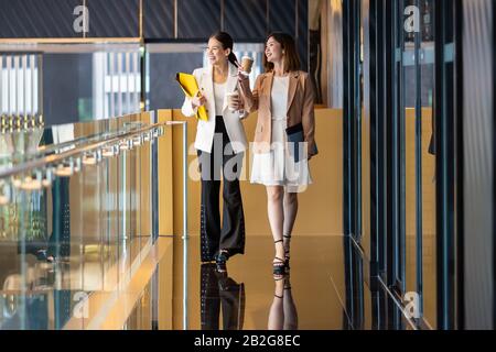 Two asian businesswomen walking and talking during coffee break in modern office or coworking space, coffee break, relaxing and talking after working Stock Photo