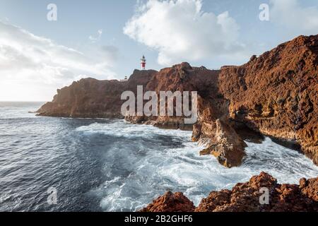 Beautiful landscape on a rocky coast with lighthouse and wavy ocean during a sunset. Teno cape on the north-west of Tenerife island Stock Photo