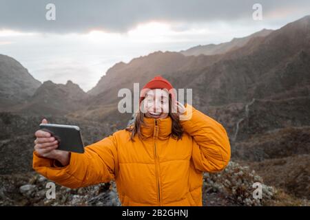 Portrait of a young traveler dressed in bright jacket and hat enjoying a trip highly in the mountains, traveling on Tenerife island, Spain