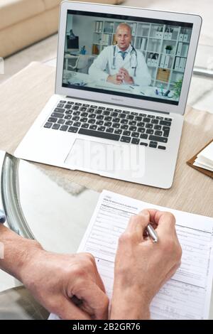 Medical specialist consulting senior man on health insurance claim online, unrecognizable senior man filling form while talking to doctor online Stock Photo