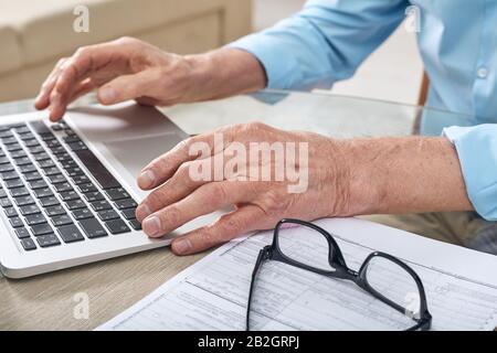 Close-up of unrecognizable elderly man sitting at table and using online service on laptop Stock Photo