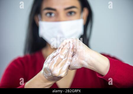 Woman wearing a face mask washing hands with soap to prevent spreading the bacterias and viruses. Corona virus concept.