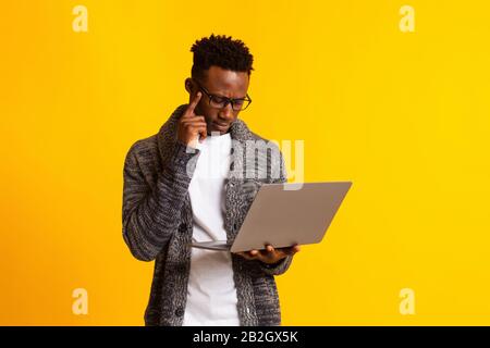 Thoughtful young afro man in glassed programming on laptop Stock Photo