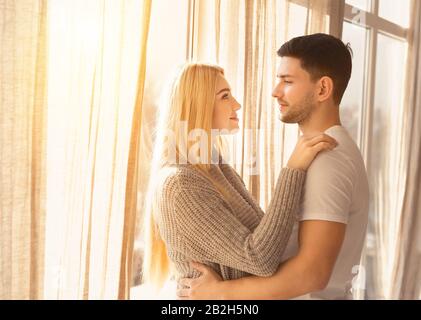 Young couple hugging near window in light room, copy space Stock Photo
