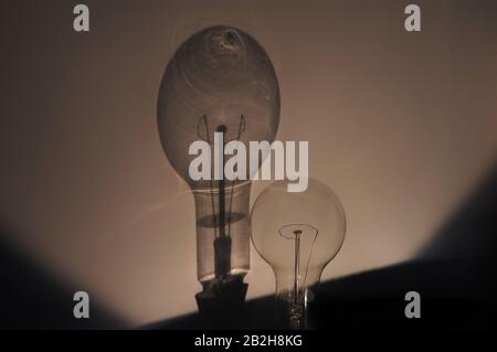 Large incandescent lightbulb lit by candlelight casting a shadow on the wall behind behind it Stock Photo