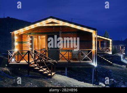 Modern wooden house decorated with yellow glowing bulbs at the mountain resort Stock Photo