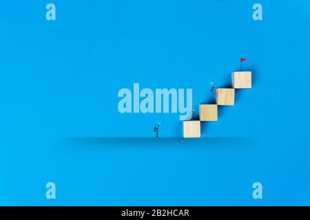 Each person's differences about success concept. A simple line art businessman going to the red flag on top of wooden block on blue background. Stock Photo