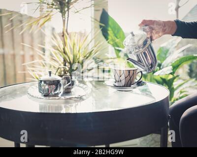 woman's hand holding hot teapot in morning sunlight, retro colors, a window through which the sun shines. Stock Photo
