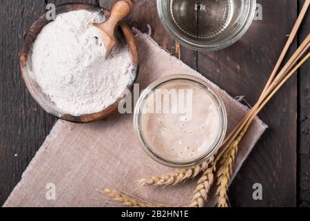 Fresh homemade bubbly sourdough starter, a fermented mixture of water and flour to use as leaven for bread baking, on wooden table Stock Photo