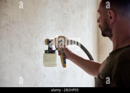 Close-up of man hands hold the tool the paint spray. Man painting with airbrush apartment repairment. House remodel. Spray paint work Stock Photo