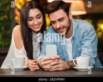 Boyfriend And Girlfriend Using Smartphone Sitting In Cafeteria Stock Photo