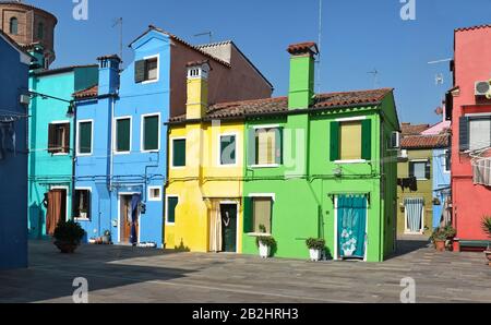 Blue, green, yellow, colourful two and three story houses of Burano, Venice on a sunny day. Curtains over doorways,shuttered windows, chimneys Stock Photo