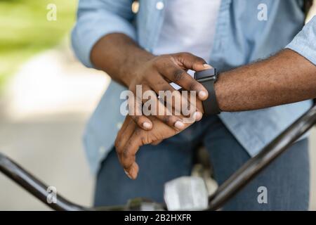 Unrecognizable afro man on bike looking at smartwatch, checking time Stock Photo