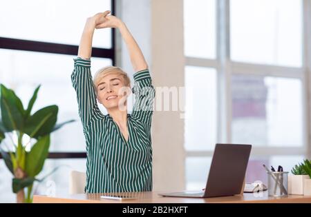 Lady Stretching Hands With Eyes Closed Working Sitting In Office Stock Photo