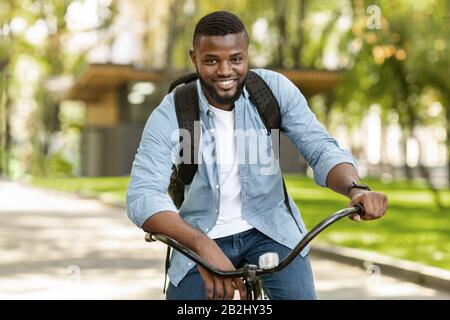 Portrait Of Handsome Afro Man Riding Bicycle Outdoors, Going To Work Stock Photo