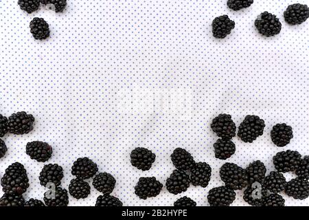 Background with a frame of fresh blackberry berries on a white background in fine polka dots. Stock Photo