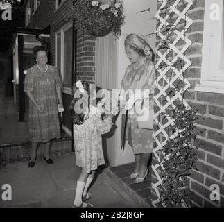 1970s, historical, a young girl presenting a flower bouquet to the the Queen mother standing in a doorway of a house as she visits a street in South London, England, UK. Stock Photo
