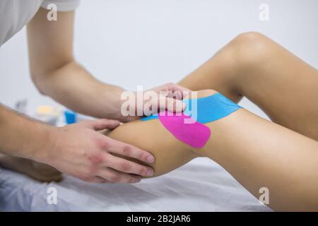 Physical therapy - therapist placing tape on patient's knee Stock Photo