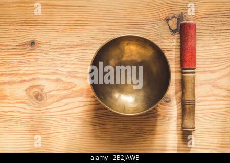 Tibetan copper bowl and wooden stick on wooden table. Stock Photo