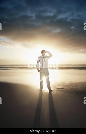 Business man standing on beach against sunset Stock Photo