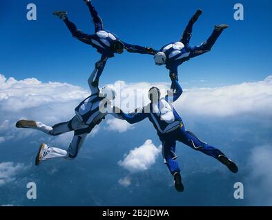 Four skydivers holding hands in ring against clouds Stock Photo