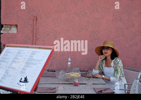 A woman sitting at an outdoor table.  Alfresco dining at Ai Cacciatori, fine dining on the islands of  Mazzorbo and Burano, Venice, Italy Stock Photo