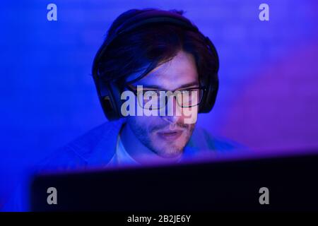 Man In Headphones Working On PC Computer Indoor At Night Stock Photo