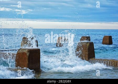 Breaking waves, water frozen in time like glass sculptural forms against the crenulated concrete walls of the Ross Jones Rockpool, Coogee bay, Sydney Stock Photo