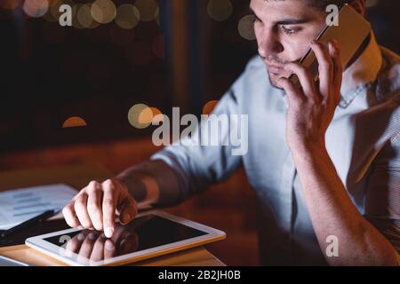 Business Guy Talking On Phone Using Tablet Overnight In Office Stock Photo