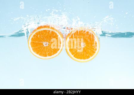 Yummy juicy orange cut in half and water splashes on blue background Stock Photo