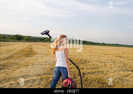 Young Woman in a Field with a Vacuum Cleaner Stock Photo
