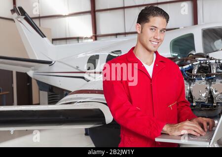 Portrait of young aeronautic engineer using laptop in front of airplane Stock Photo