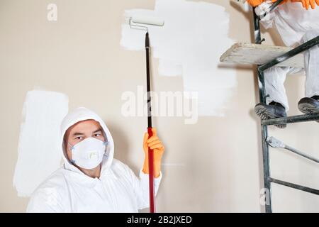 Portrait of male worker holding paint roller with female worker sitting on scaffold Stock Photo