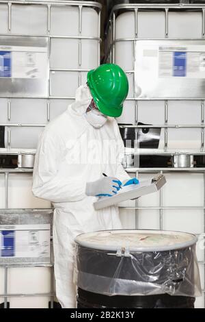 Technician in hazmat suit taking down notes of chemical in drum Stock Photo
