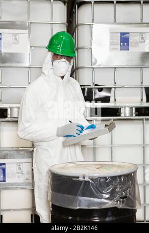 Male technician in hazmat suit taking down notes of chemical in drum Stock Photo