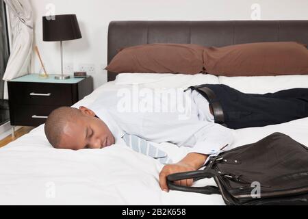Tired young African American businessman sleeping in bed Stock Photo