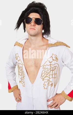 Portrait of Elvis impersonator in white jump suit with hands on hips against gray background Stock Photo