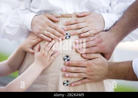Belly of a pregnant woman. Hands of husband and older child on belly. The concept of the family, the child's expectations and love. Stock Photo