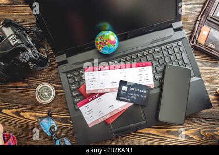 Preparing for an exciting journey. Booking flights and paying with a credit card using a laptop on a wooden background. The view from the top. Stock Photo