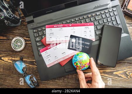 Preparing for an exciting journey. Man books flights by typing on a laptop and paying with a credit card on a wooden background. The view from the top Stock Photo