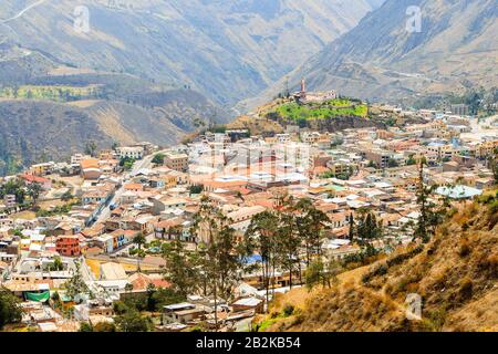 An aerial perspective of a densely built town situated in a mountain valley. The settlement features numerous closely packed buildings with varied roof colors, including red, blue, and gray Stock Photo