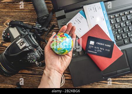 Preparing for an exciting journey. Man books flights by typing on a laptop and paying with a credit card on a wooden background. The view from the top Stock Photo