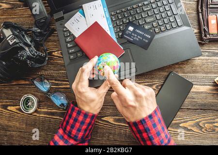Preparing for an exciting journey. Man books flights by typing on a laptop and paying with a credit card on a wooden background. The view from the top Stock Photo
